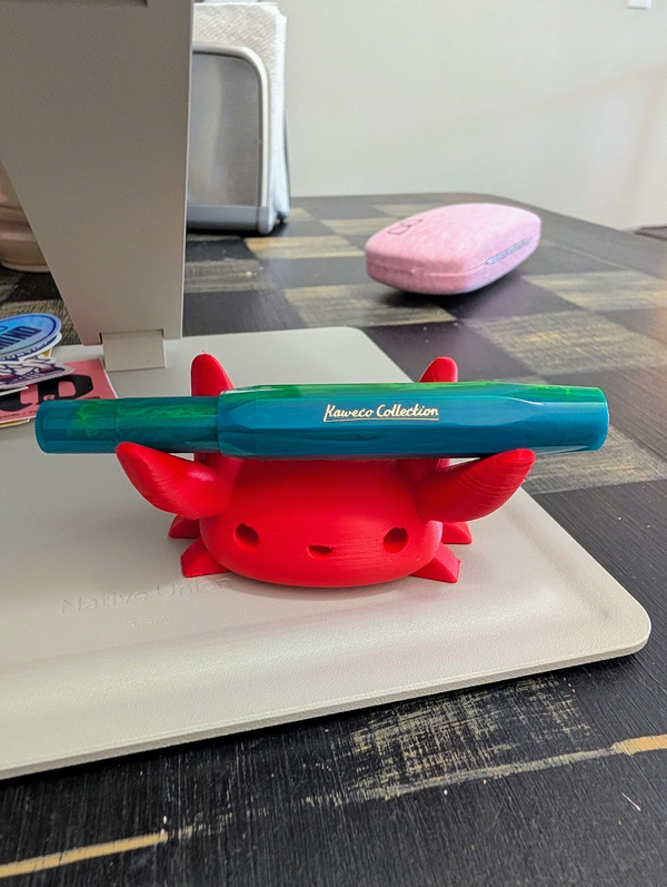 Red 3D-printed crab pen holder on a desk mat, holding a teal Kaweco Collection fountain pen